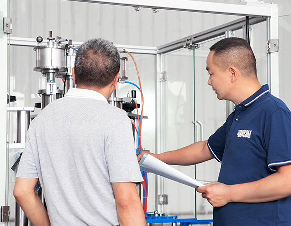 An engineer is teaching a worker how to use the aerosol filling machine